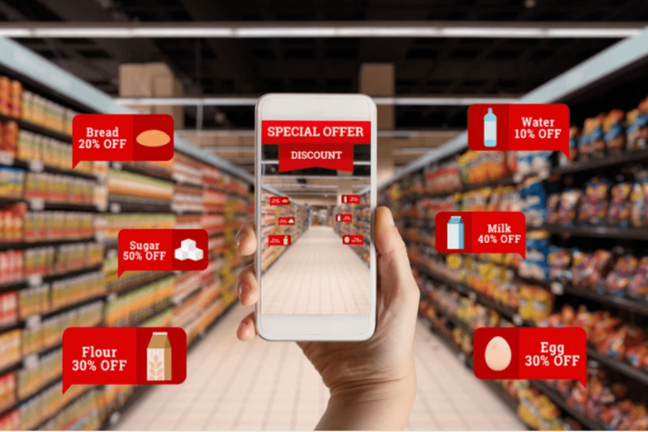 A person holding a smartphone in a grocery store aisle. The phone's screen displays a virtual view of the aisle with augmented reality overlays showing product information and discounts for various items, including bread, water, sugar, milk, flour, and eggs.